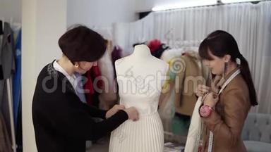 两个专业的裁缝，设计师与新的模型裁剪白色连衣裙在人体模型在工作室，阿泰利尔。 修复