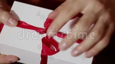 美丽的女孩打开她的礼物。 美丽的双手打开一个女孩`新年礼物，解开一条红丝带。 假期的礼物。 礼品