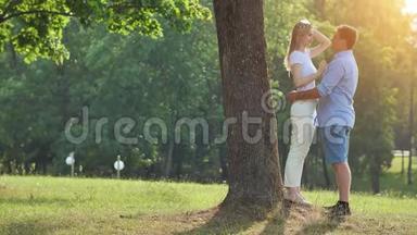 一个年轻的男人和女人站在公园的一棵树<strong>下</strong>拥抱。