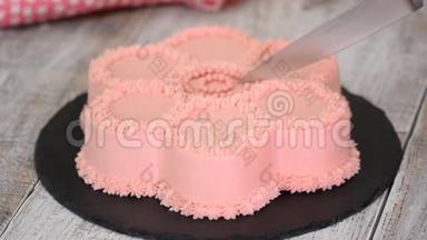 女人`她的手用粉红色奶油把蛋糕切成一朵花的形状。