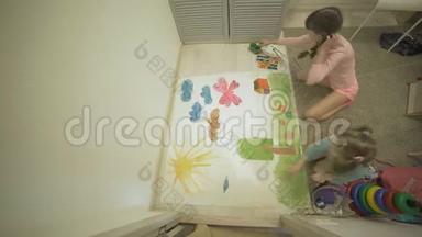 两个女孩在地板上用水彩颜料和画笔在一张大画纸上画画，孩子们`共同的创造力。