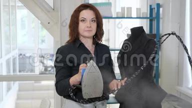 无缝的女人，手里拿着铁，在裁缝车间看着相机。