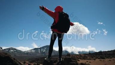 年轻女子徒步旅行者双手背着黑色背包，在蓝天和蓝天的映衬下，双手撑在山顶上