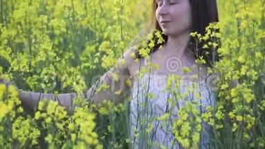 一个迷人的女人走过一片黄色的油菜地。 女孩安息在清新的空气中，美丽的夏日风景..