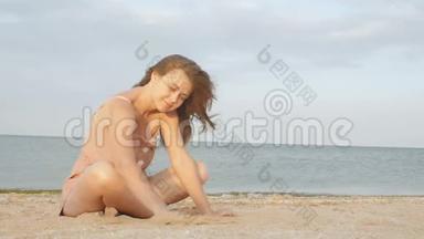年轻快乐的女孩坐在岸边<strong>玩沙子</strong>，一个女人拿着一把<strong>沙子</strong>，洒在风中，度假的同事