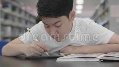亚洲预科男孩使用平板电脑在图书馆。 两个男孩微笑着在平板电脑上画画。