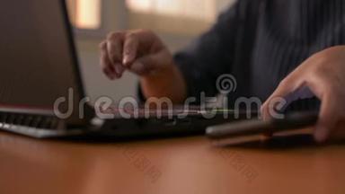 女人的手在电脑键盘上打字，用手机，女商人在办公室里用笔记本电脑工作。