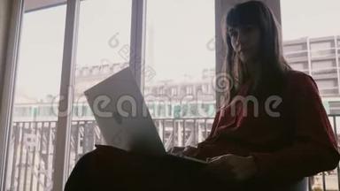 快乐美丽的年轻女商人微笑着使用笔记本电脑在巴黎的公寓窗口，<strong>火车经过</strong>。