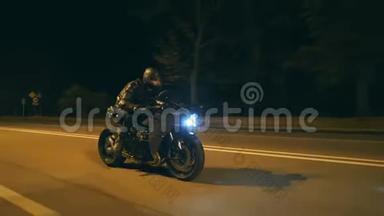 戴头盔的年轻人骑着现代黑色摩托车在傍晚的城市街道。 他的摩托车手