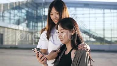 两个<strong>活泼</strong>可爱的年轻亚洲女孩，在现代建筑附近的电话中，微笑着修改<strong>有趣</strong>的照片