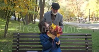 快乐的老夫妻正坐在秋天舒适的城市公园里的长凳上。 使用手机的男人