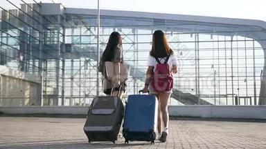 机场大楼附近，两位留着长头发的年轻亚裔黑发女郎带着<strong>行李箱</strong>。