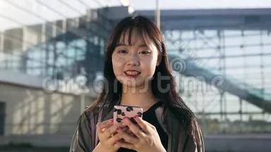 长着长发、手持手机、看着现代机场附近的摄像机的亚洲黑发美女