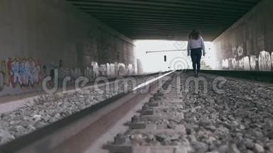年轻女子走在充满涂鸦的隧道中的火车轨道之间。 慢动作