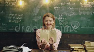 女人微笑着。 女老师手里拿着书，在绿色的学校董事会背景上微笑。 学校背景