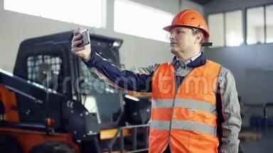 戴着头盔和工作服的导演站在新的工作设备旁边，在他的手机上拍了一些照片。