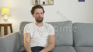无聊的男人独自坐在房间里的沙发上看电视，手里拿着遥控器，<strong>切换</strong>频道