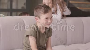 笑的<strong>小</strong>男孩坐在前景的沙发上的肖像。 <strong>姐姐</strong>和哥哥在后台玩