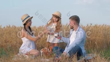 家庭草地野餐，小女孩把牛奶倒进她父母的眼镜，他们交流喝牛奶一边喝牛奶