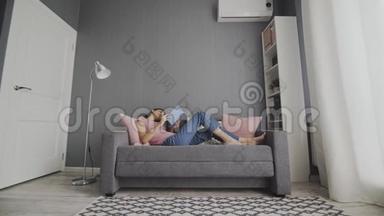 睡懒觉的女人躺在沙发上在家看无聊的书。 大学生在沙发上学习看<strong>课本</strong>觉得无聊