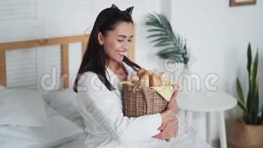 穿着<strong>白色浴袍</strong>的年轻女子手里拿着一篮子面包，微笑着
