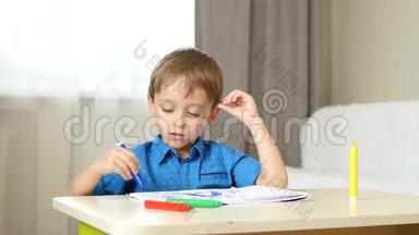一个小男孩坐在房间里的桌子旁<strong>画画</strong>，想象着一个家庭。 孩子<strong>画画</strong>。 情绪：快乐
