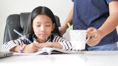 母亲给女儿一个白色的杯子，亚洲小女孩在做家庭作业时，快乐地自学和<strong>家庭教育</strong>