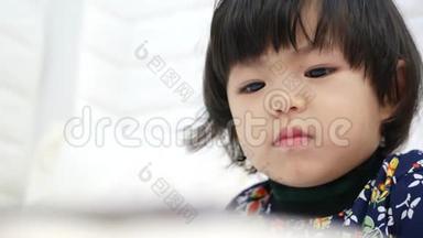 当一个2岁的亚洲小女孩在家看智能手机时，她正全神贯注地`她的脸