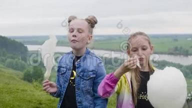 两个十几岁的女孩在<strong>夏</strong>天的森林和河流景观上吃甜棉花。 带着<strong>甜美</strong>棉花的女朋友