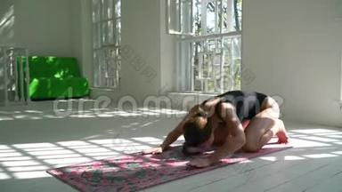 美丽的年轻健康的白种人女人在白色的大房间里的<strong>垫子</strong>上练习瑜伽。 体育运动中的年轻妇女