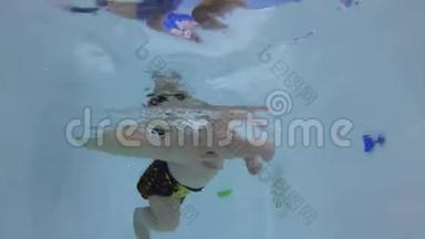 快乐的宝宝在游泳池的水下潜水.. 宝贝学习游泳。 未编辑的水下录像。