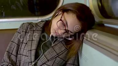 一个年轻的女人在地铁火车上睡着了。 戴着耳机的女孩。 旧地铁车