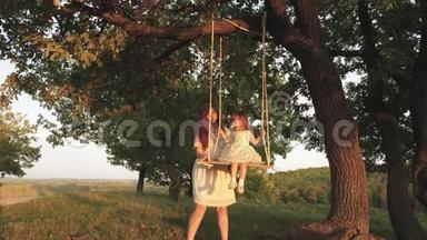 快乐的妈妈把一个快乐的女儿卷在橡树上的公园里的秋千上。 幸福家庭的概念.. 单身母亲