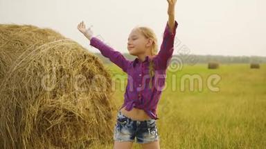 快乐的女孩在干草堆背景上伸手到天空。 少女在收获时举手享受大自然