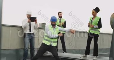 有魅力的工程师，留着胡子，在休息时间在建筑屋顶的同事面前跳舞