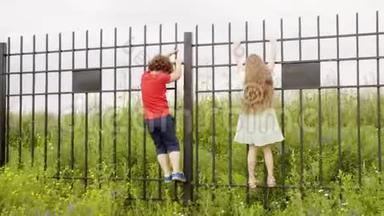 农村的小男孩和小女孩爬上铁栅栏。 <strong>孩子</strong>们<strong>暑假</strong>在村里玩得很开心。