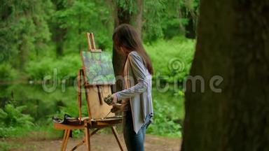 一位年轻的艺术家女士在夏林中画一幅<strong>风景画</strong>的后中景
