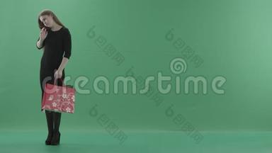 美丽快乐的女人穿着小<strong>黑裙子</strong>，摆着购物袋，在手机上说话。 她是