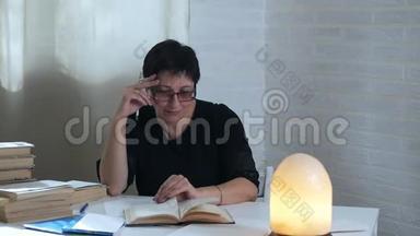 女人翻阅一本悠闲的书，坐在昏暗的灯光背景下的白色桌子旁
