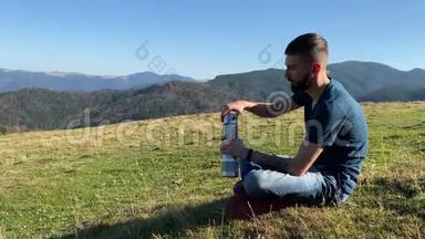 一个年轻人从<strong>热水</strong>瓶里<strong>喝</strong>茶，看着山。