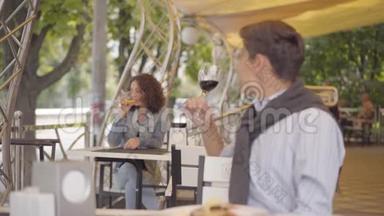 英俊的男人喝着红酒坐在前台，举起酒杯看着坐在前台的漂亮女人