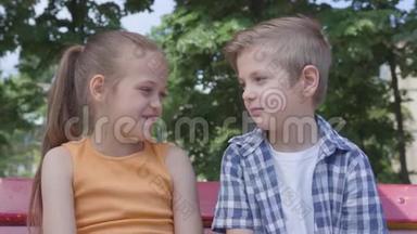 可爱的男孩和可爱的女孩坐在公园里的秋千上，聊天跳舞，玩得很开心。 一对快乐