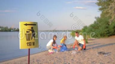 垃圾桶上的指针标志带着小孩的年轻家庭在肮脏的沙滩上用塑料收集垃圾