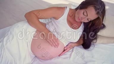 孕妇躺在床上抚摸着一个大肚子。