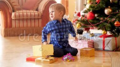 4k视频愤怒的男孩坐在圣诞树下大喊，因为他点了不需要的礼物和礼物