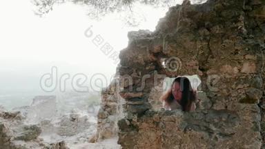 旅游妇女透过窗户四处张望，这座古老的山城的建筑被毁坏了。走进来的旅游妇女