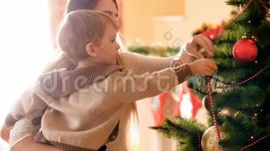 4k的<strong>小男孩帮助</strong>他妈妈用圣诞饰品和玩具装饰圣诞树的镜头。家庭准备和