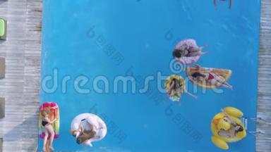 在夏季游泳池休息，一群女孩朋友穿着泳衣在游泳池边的充气圈和床垫上游泳