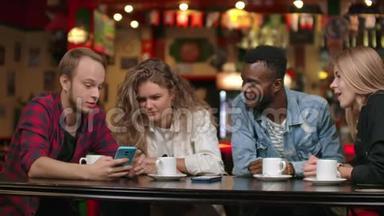 在酒吧里，一群快乐的朋友一边喝着咖啡一边笑着讨论着看着智能手机屏幕