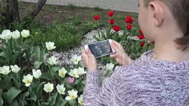 一个十几岁的男孩在春天的花园里用智能<strong>手机制作</strong>郁金香花的视频或照片